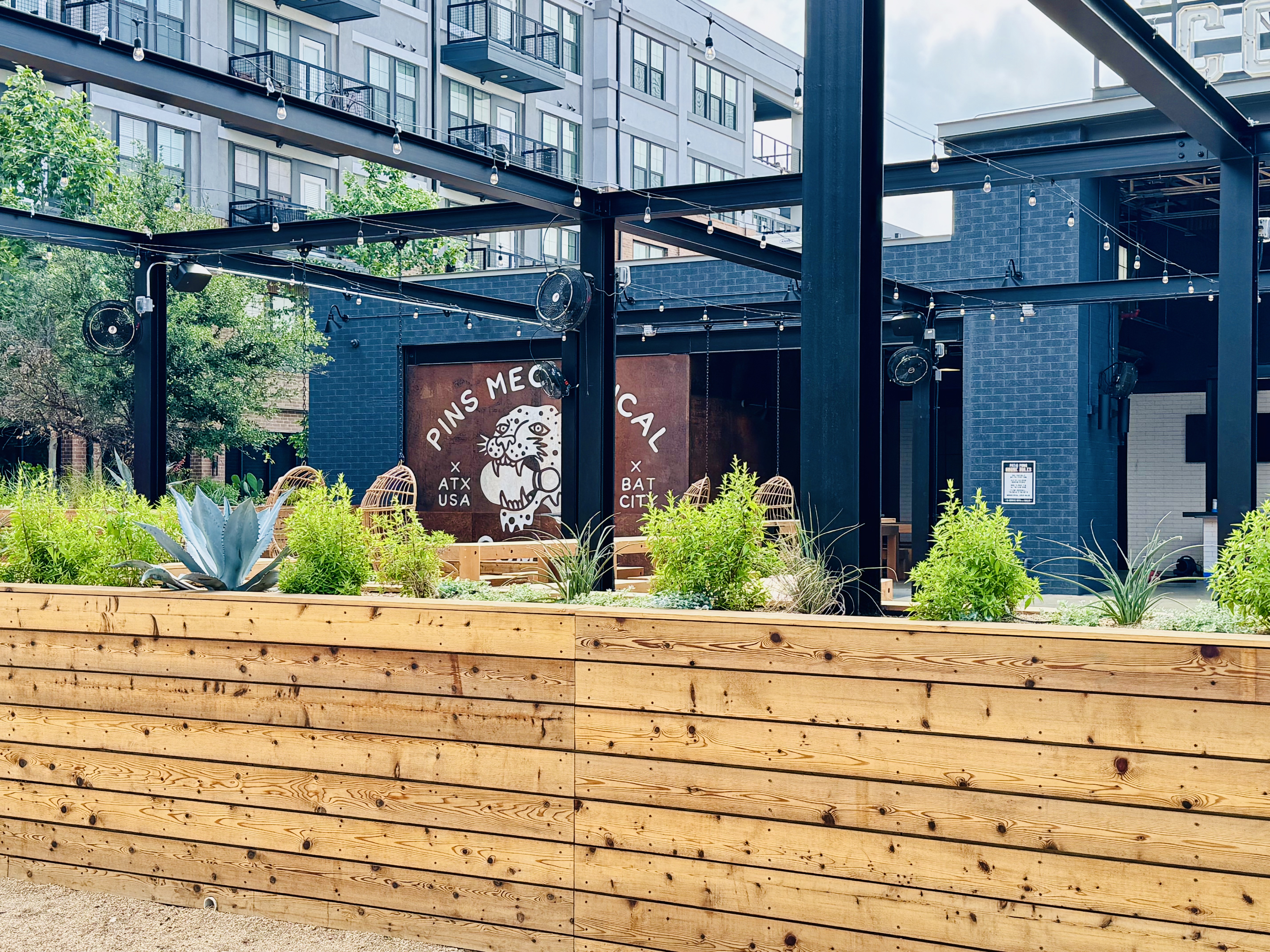 The planter wall in full sun, agave and grasses above the cedar, hanging chairs beyond